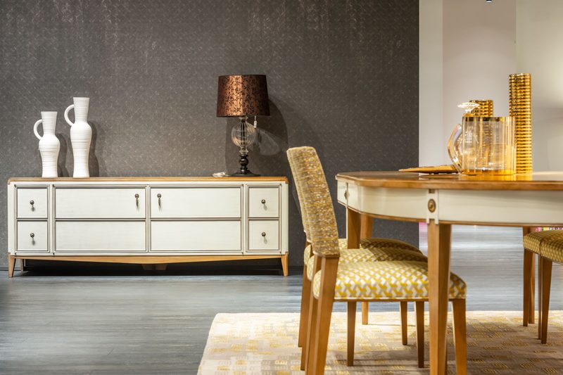 Dining area with a dark textured wallcovering behind an ivory sideboard and a round wooden table