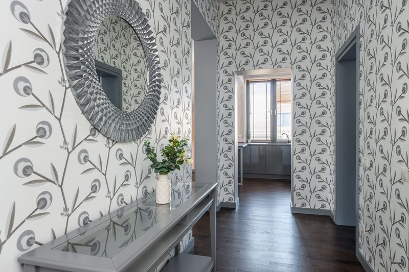 Hallway papered in grey botanical wallpaper with a sunburst mirror above a console table