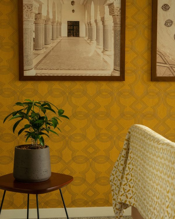 Living room corner with ochre trellis wallpaper, framed architectural prints and a potted plant