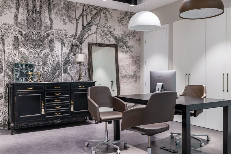 Home office with a grey engraved-forest mural wallpaper behind a black sideboard and a desk