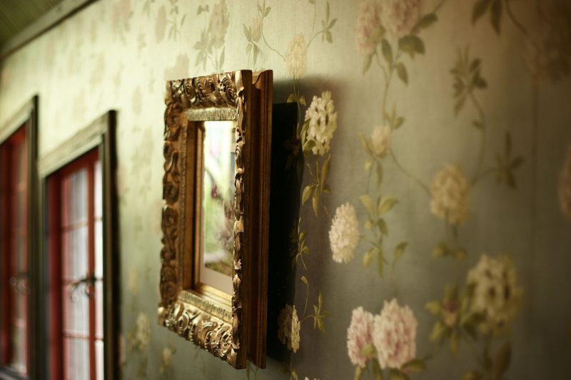 Olive-green floral wallpaper with pale hydrangea blooms, a carved gilt frame and red-trimmed windows
