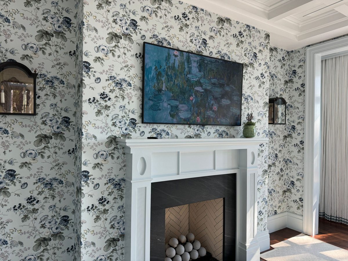 Living room with blue-grey floral wallpaper wrapping the walls around a white fireplace mantel and a framed painting