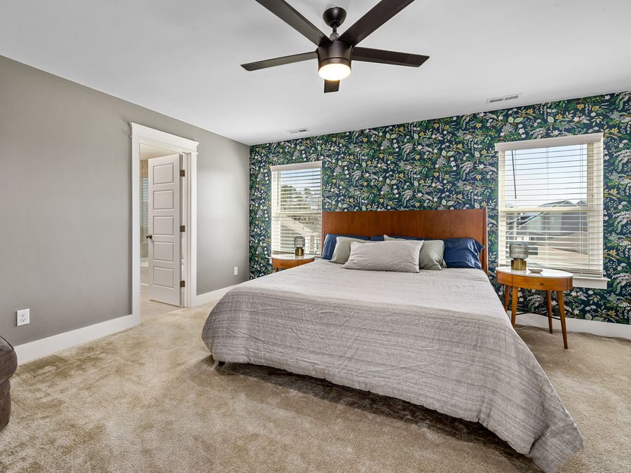 Bedroom with a dark green botanical wallpaper accent wall behind the bed and between two windows