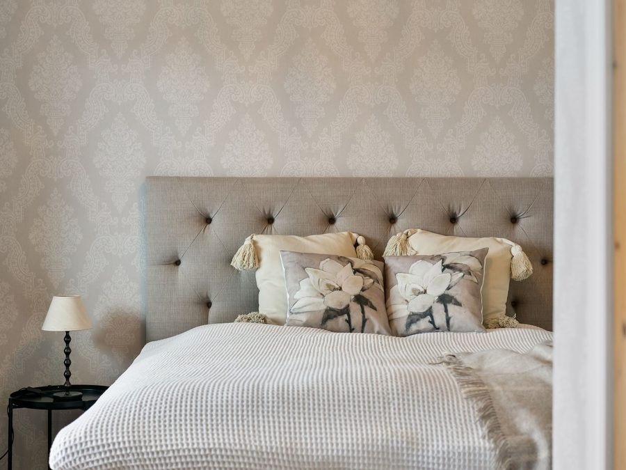 Calm bedroom with beige damask wallpaper behind a tufted linen headboard