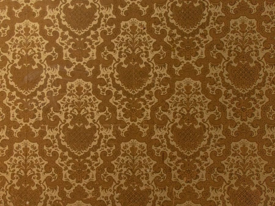 Close-up of brown damask wallpaper on a textured wall surface